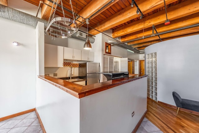 kitchen with white cabinets, a sink, freestanding refrigerator, and baseboards