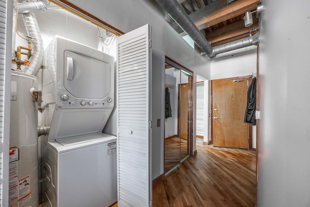 washroom with wood finished floors, stacked washer and clothes dryer, water heater, and laundry area