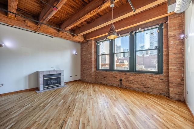 unfurnished living room featuring baseboards, a tile fireplace, brick wall, wood finished floors, and beam ceiling