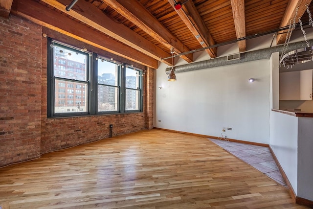 spare room with brick wall, wood finished floors, visible vents, baseboards, and beam ceiling