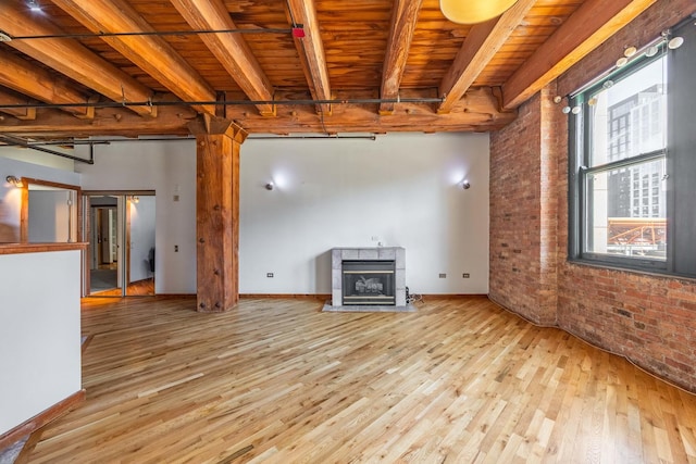 unfurnished living room featuring brick wall, beamed ceiling, a tiled fireplace, and wood finished floors