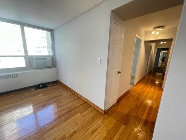 spare room featuring baseboards, cooling unit, light wood-style flooring, and radiator