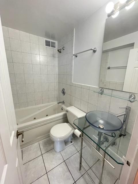 full bathroom featuring toilet, a sink, tile walls,  shower combination, and tile patterned floors