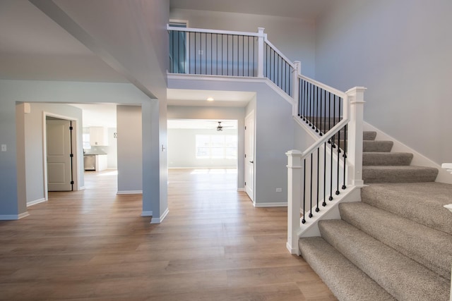 stairs with a ceiling fan, a high ceiling, baseboards, and wood finished floors