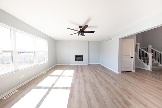 unfurnished living room with a glass covered fireplace, visible vents, stairway, and light wood finished floors