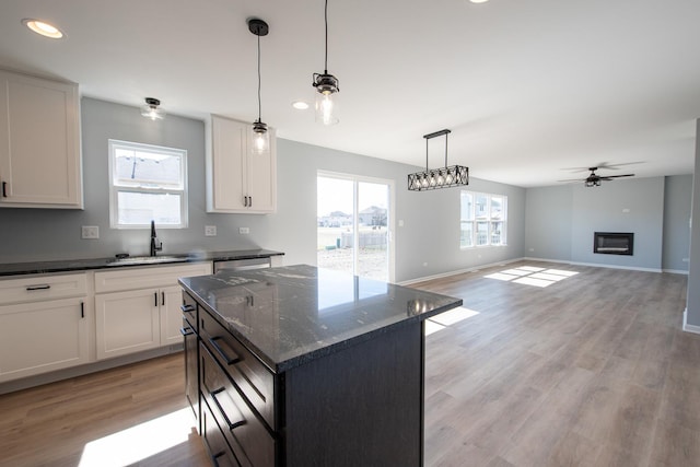 kitchen with light wood-style floors, a glass covered fireplace, white cabinetry, a sink, and ceiling fan