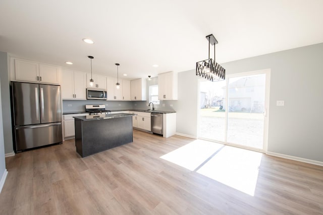 kitchen with dark countertops, appliances with stainless steel finishes, white cabinetry, a kitchen island, and light wood-type flooring