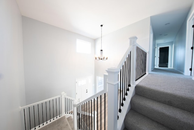 stairway with carpet floors and an inviting chandelier