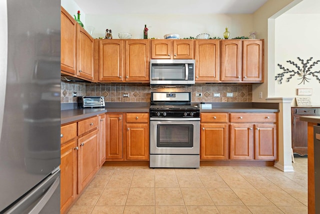 kitchen featuring appliances with stainless steel finishes, dark countertops, light tile patterned floors, and tasteful backsplash