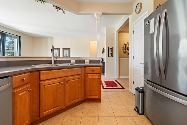 kitchen featuring light tile patterned floors, decorative columns, brown cabinetry, appliances with stainless steel finishes, and a sink