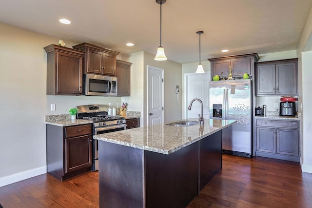 kitchen with dark wood-style flooring, appliances with stainless steel finishes, a sink, dark brown cabinets, and light stone countertops