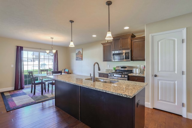 kitchen featuring dark wood finished floors, appliances with stainless steel finishes, light stone countertops, pendant lighting, and a sink