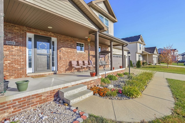 view of exterior entry with a garage, covered porch, a residential view, and brick siding