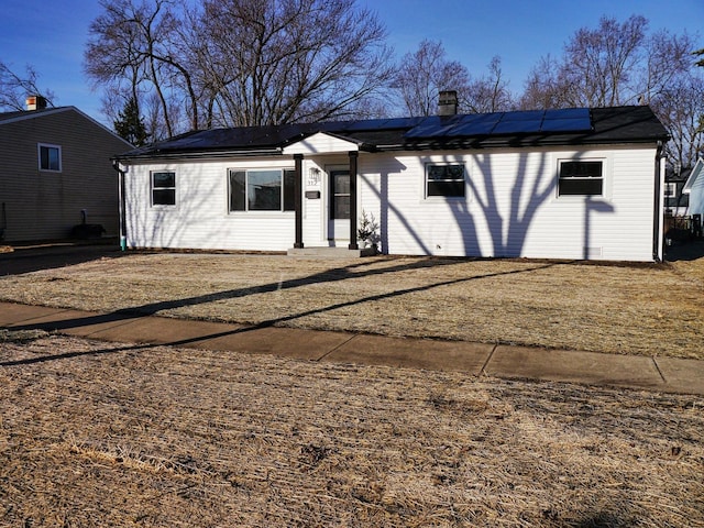 ranch-style home with roof mounted solar panels and a chimney