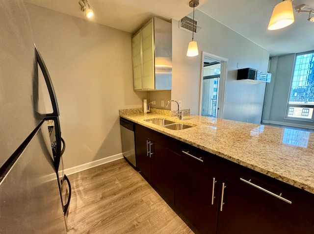 kitchen with stainless steel appliances, a sink, light stone countertops, light wood-type flooring, and baseboards