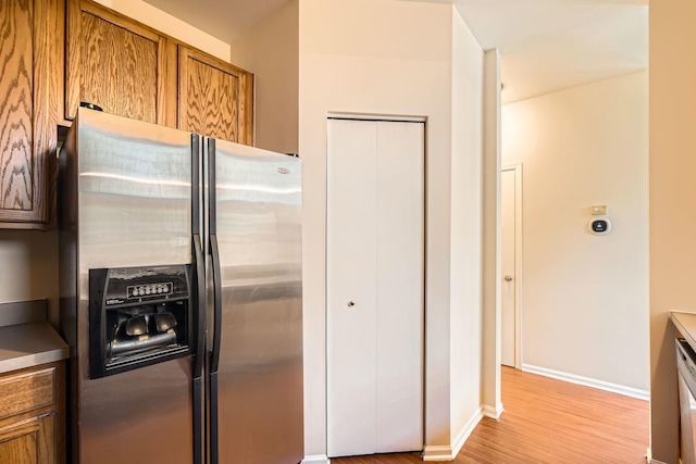 kitchen featuring light wood finished floors, baseboards, brown cabinetry, and stainless steel fridge with ice dispenser