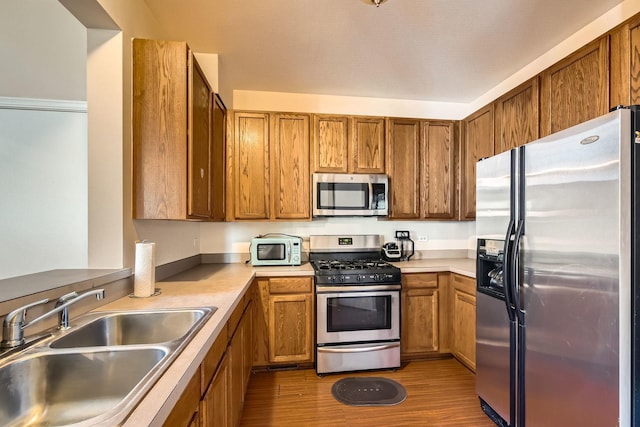 kitchen featuring brown cabinets, stainless steel appliances, a sink, and wood finished floors