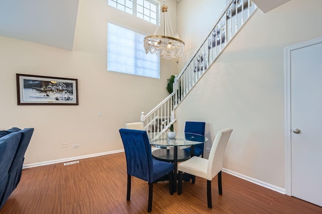 dining area with wood finished floors, a towering ceiling, baseboards, stairs, and an inviting chandelier