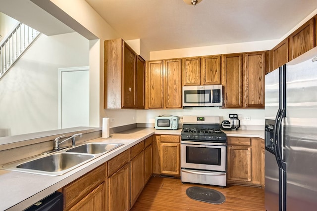 kitchen featuring stainless steel appliances, wood finished floors, brown cabinetry, and a sink