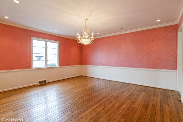 empty room featuring hardwood / wood-style flooring, a notable chandelier, visible vents, and crown molding