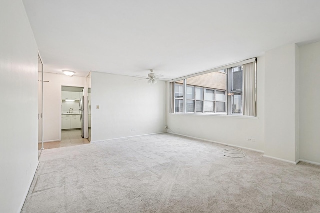 carpeted empty room with a ceiling fan, a sink, and baseboards