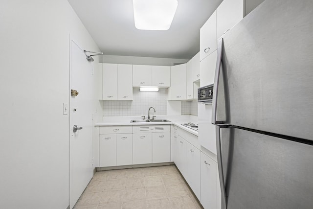 kitchen featuring a sink, white cabinets, light countertops, freestanding refrigerator, and decorative backsplash