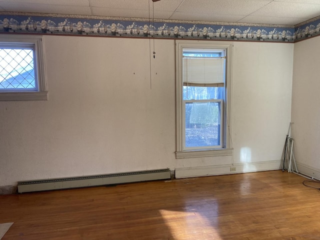 empty room featuring a paneled ceiling, plenty of natural light, a baseboard heating unit, and wood finished floors