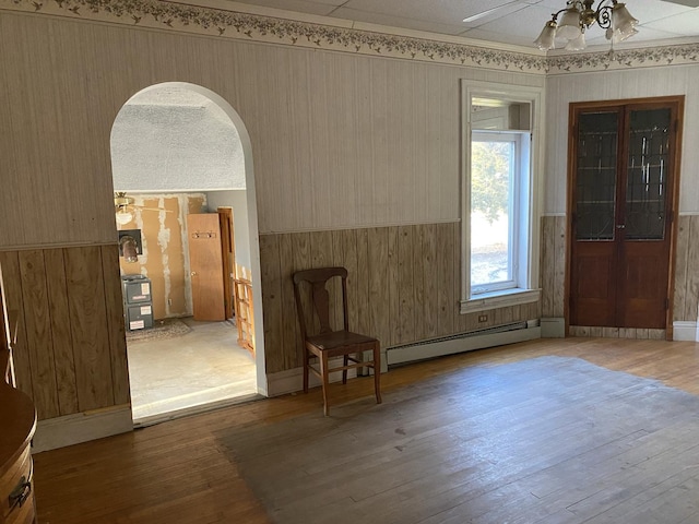 interior space with arched walkways, ceiling fan, baseboard heating, and wood finished floors