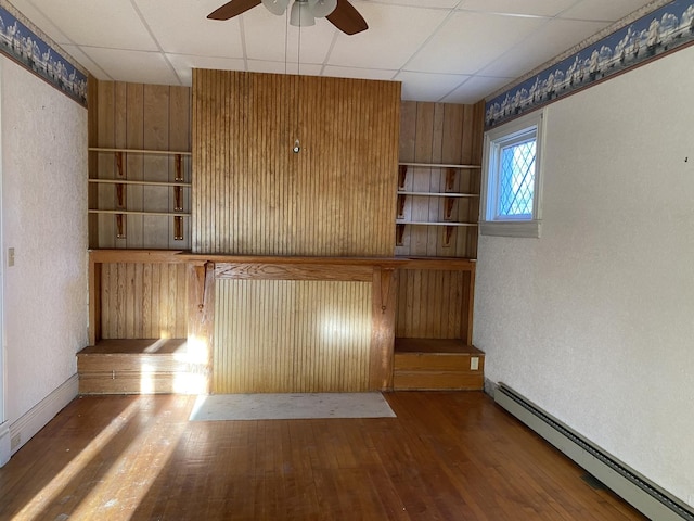 unfurnished office with a baseboard heating unit, a drop ceiling, ceiling fan, and hardwood / wood-style floors