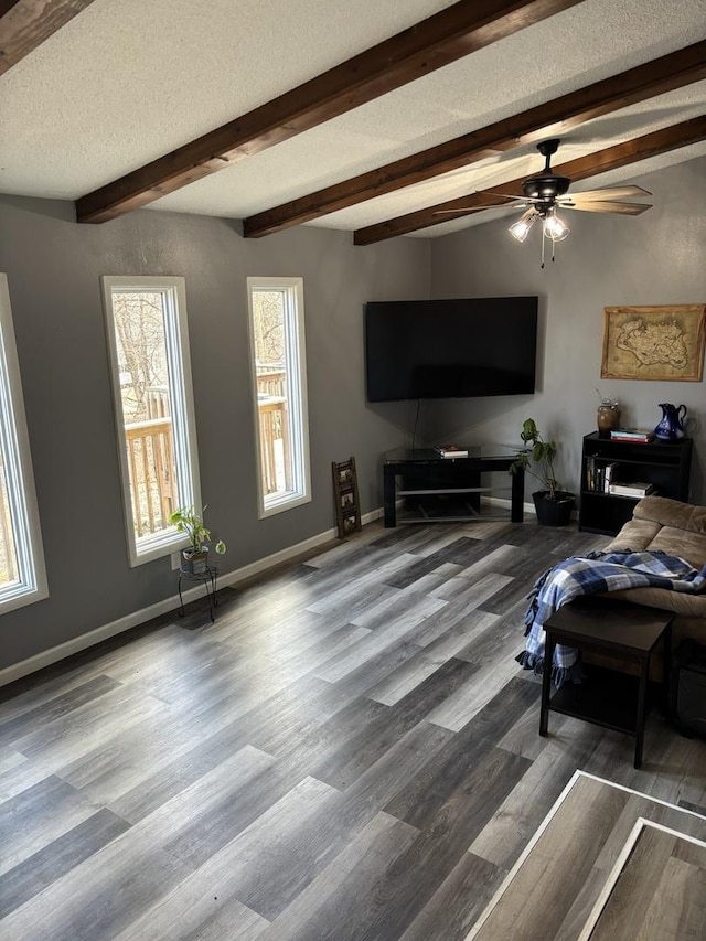 living area featuring baseboards, a ceiling fan, beamed ceiling, wood finished floors, and a textured ceiling