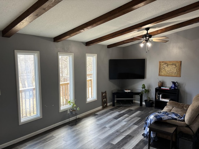 living area with beam ceiling, a ceiling fan, a textured ceiling, wood finished floors, and baseboards