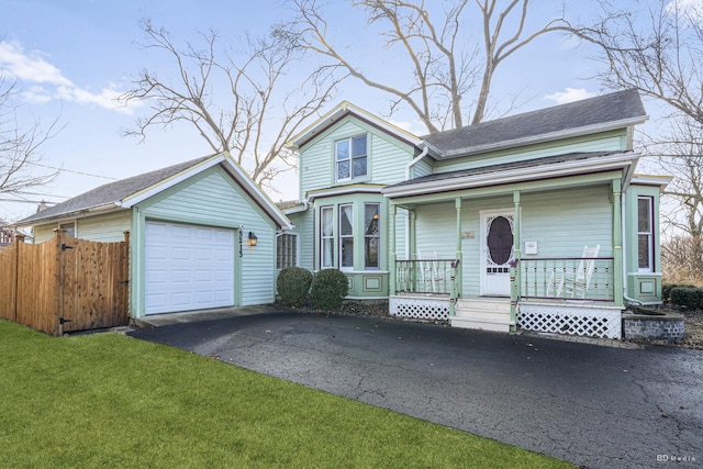 view of front of house featuring a detached garage, aphalt driveway, covered porch, fence, and a front yard