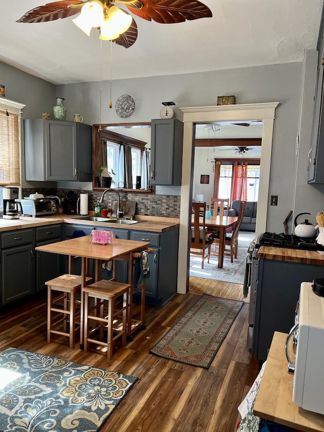 kitchen with range with gas cooktop, dark wood-style flooring, backsplash, a sink, and butcher block countertops