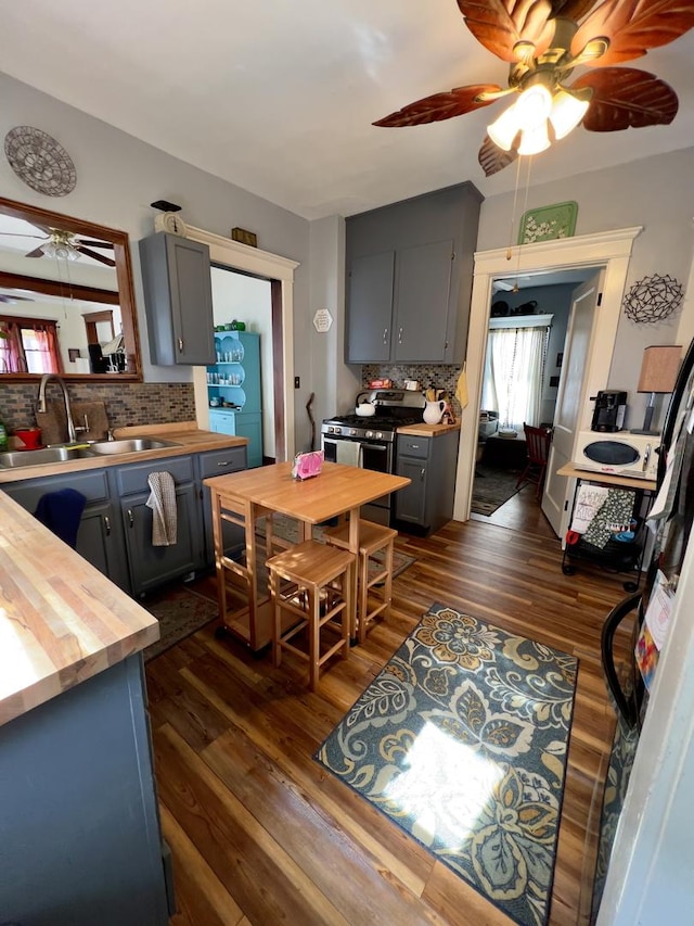 kitchen featuring stainless steel gas range oven, dark wood-type flooring, butcher block counters, a sink, and gray cabinets