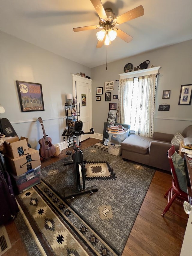 living area featuring a ceiling fan, visible vents, baseboards, and wood finished floors