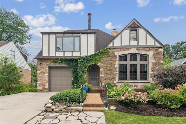 tudor home with a garage, brick siding, driveway, stucco siding, and a chimney