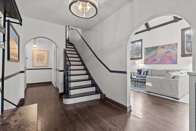 staircase featuring baseboards, arched walkways, and wood finished floors