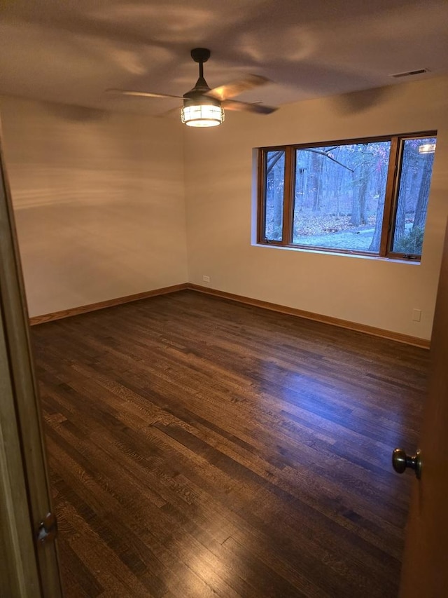 unfurnished room with dark wood-style floors, visible vents, baseboards, and a ceiling fan