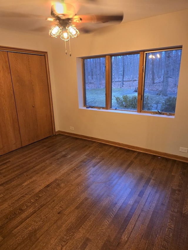 unfurnished bedroom with a ceiling fan, a closet, baseboards, and dark wood-style flooring