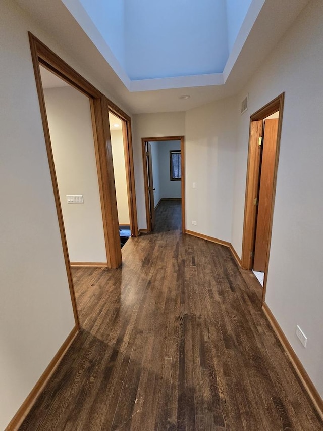 hall with a towering ceiling, baseboards, visible vents, and wood finished floors