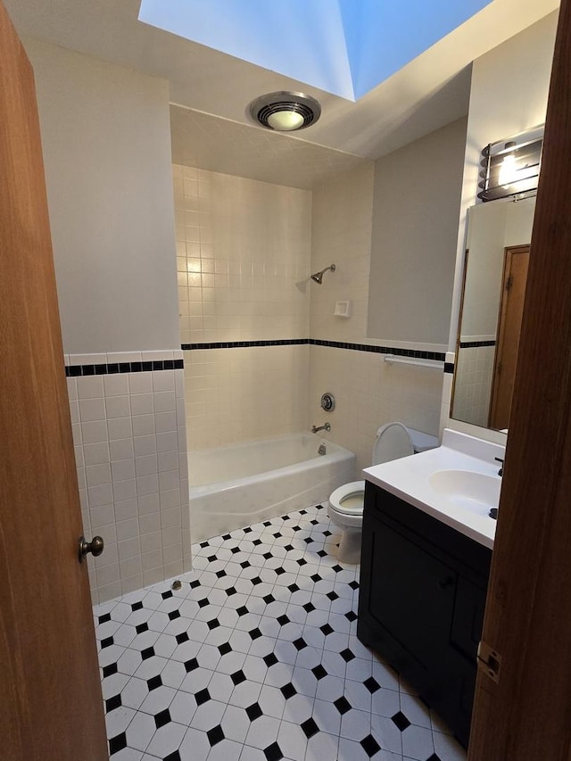 bathroom with tile walls, toilet, wainscoting, tub / shower combination, and vanity