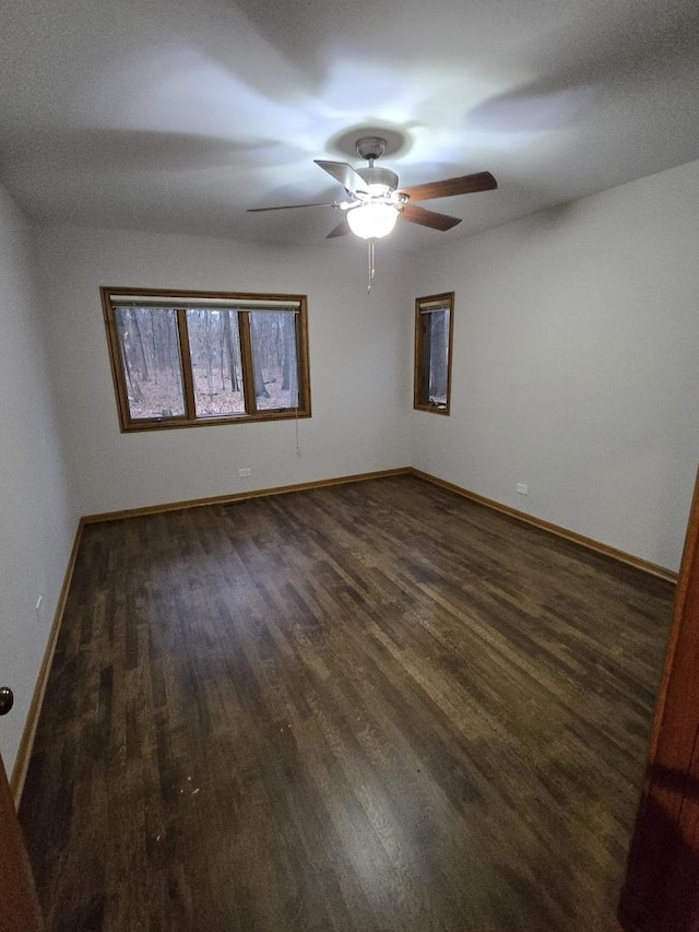 empty room featuring a ceiling fan, baseboards, and dark wood-type flooring