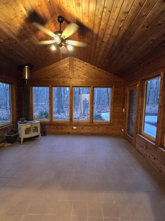 unfurnished living room with vaulted ceiling, wooden ceiling, a wood stove, and a ceiling fan