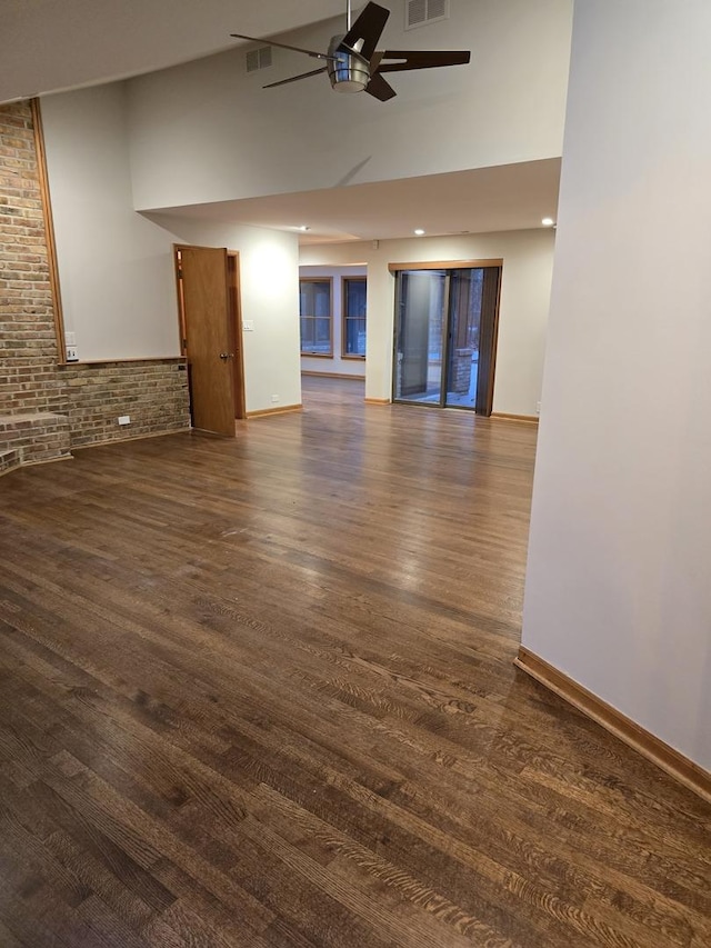 unfurnished living room with brick wall, ceiling fan, visible vents, and dark wood finished floors