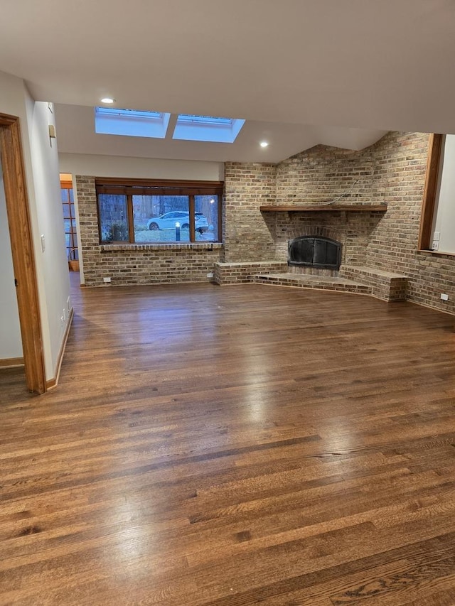 unfurnished living room with dark wood-style floors, brick wall, a brick fireplace, and recessed lighting