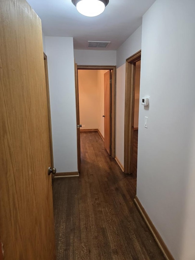 hall with baseboards, visible vents, and dark wood finished floors