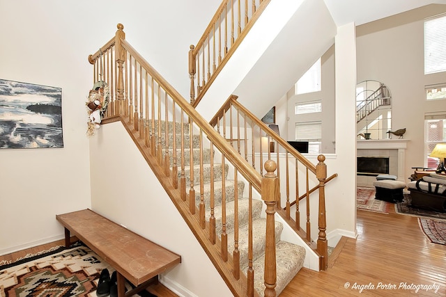 staircase with a tile fireplace, a towering ceiling, baseboards, and wood finished floors