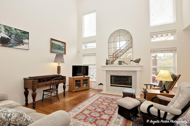 living room with baseboards, a towering ceiling, a tiled fireplace, and wood finished floors