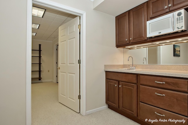 kitchen featuring white microwave, baseboards, light countertops, and a sink