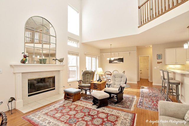 living area featuring light wood-style floors, a tile fireplace, a high ceiling, and baseboards